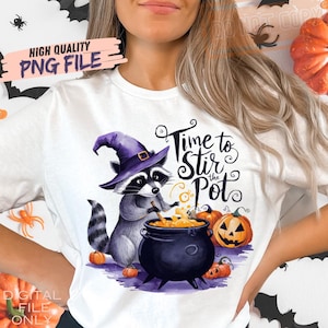 May include: White t-shirt featuring a Halloween-themed graphic. The design includes a raccoon wearing a purple witch hat, stirring a cauldron with the text "Time to Stir the Pot." Pumpkins and the words "High Quality PNG File" are also visible.