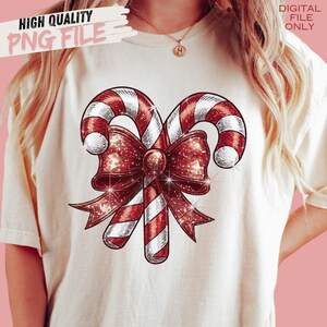 Op de afbeelding: Cr&egrave;mekleurig T-shirt met een feestelijk ontwerp van twee zuurstokken met rood-witte strepen, verweven met een sprankelende rode strik. De woorden "HIGH QUALITY PNG FILE" en "DIGITAL FILE ONLY" staan op het shirt.