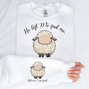 K&ouml;nnte beinhalten: Wei&szlig;er Pullover mit einem schwarzen und braunen Comic-Schaf und dem Text "He left 99 to find me. But now, I am found."