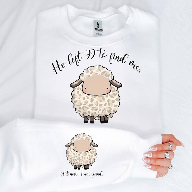 K&ouml;nnte beinhalten: Wei&szlig;er Pullover mit einem schwarzen und braunen Comic-Schaf und dem Text "He left 99 to find me. But now, I am found."