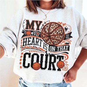 May include: A grey sweatshirt with the text "My heart is on that court" printed on it. The text is surrounded by a black and white leopard print basketball, hearts, and floral designs.