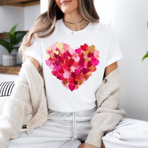 May include: White t-shirt with a large heart design made up of many smaller pink, red, and gold hearts.