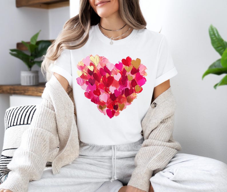 May include: White t-shirt with a large heart design made up of many smaller pink, red, and gold hearts.