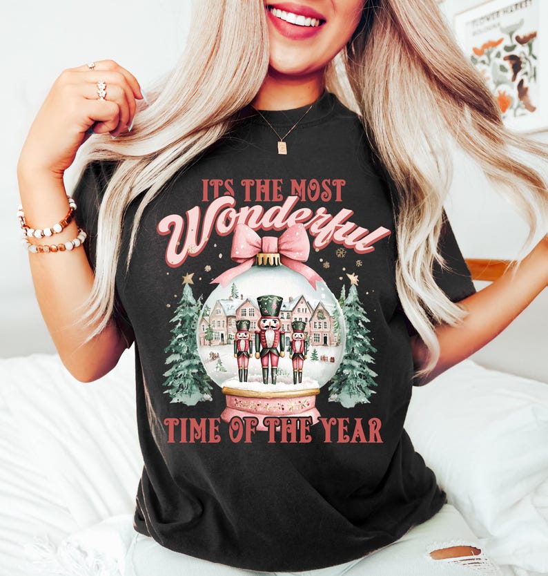 May include: Black t-shirt with a pink and white Christmas design. The design features a snow globe with three nutcracker figures inside. The text "It's the most Wonderful Time of the Year" is printed on the shirt.