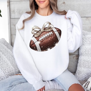 Pode incluir: Camisola branca com uma bola de futebol castanho e dourado com glitter e um la&ccedil;o branco no topo.