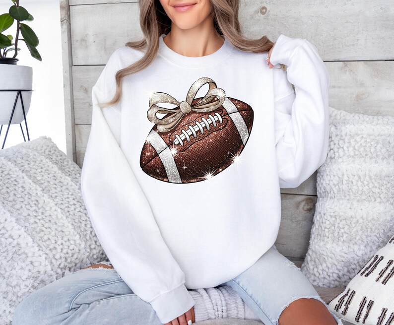 Pode incluir: Camisola branca com uma bola de futebol castanho e dourado com glitter e um la&ccedil;o branco no topo.