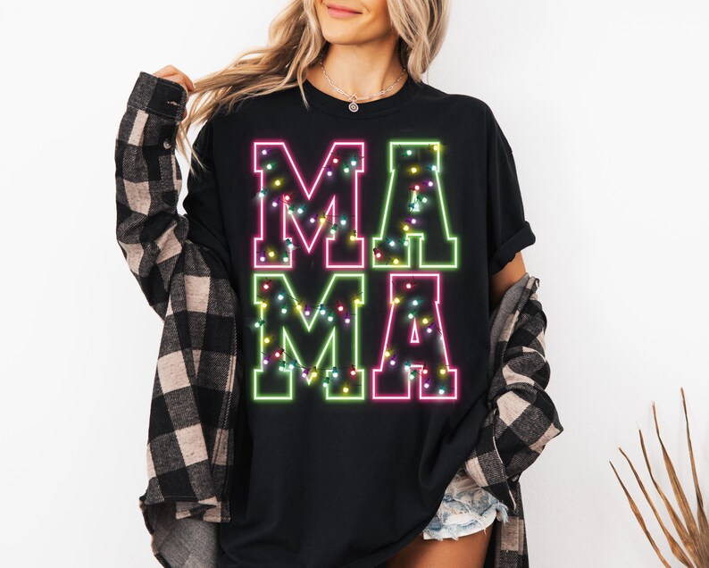 May include: Black t-shirt with the word "MAMA" in large, neon-style letters. The letters are outlined in green and pink, with a string of colorful lights inside each letter. The shirt is a casual, everyday wear item.