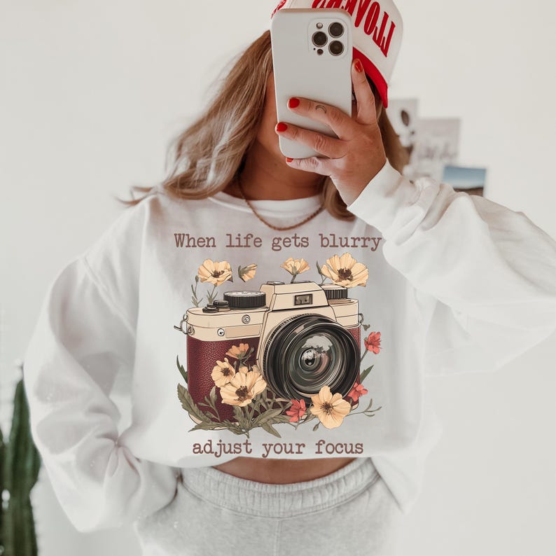 May include: White sweatshirt with a vintage camera graphic and the text "When life gets blurry adjust your focus".