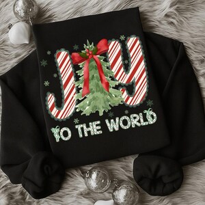 Puede incluir: Sudadera negra con un dise&ntilde;o navide&ntilde;o. La palabra "JOY" est&aacute; en rayas rojas y blancas de bast&oacute;n de caramelo, con un &aacute;rbol de Navidad verde y un lazo rojo. La frase "TO THE WORLD" est&aacute; en verde, con copos de nieve.