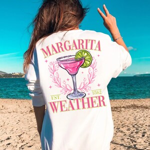 May include: White sweatshirt with a pink margarita graphic and the text "Margarita Weather" with the year "1862" and "Est." printed below.