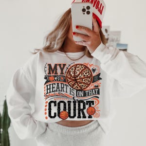 May include: White sweatshirt with a graphic print of a basketball with a leopard print design. The text on the graphic says "My heart is on that court".