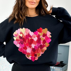 May include: Black sweatshirt with a large heart design made of many smaller painted hearts in shades of pink, red, and gold.