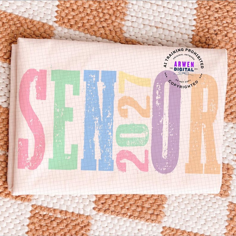 Puede incluir: Una tela rosa claro con un patr&oacute;n de cuadr&iacute;cula y la palabra SENIOR 2027 impresa en letras de bloque grandes, desgastadas y multicolores que incluyen rosa, verde, azul, amarillo y naranja. Un logotipo circular con el texto ARWEN DIGITAL es visible.