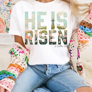 May include: White t-shirt with a floral design that spells out "He is Risen" with the scripture reference "Matthew 28:6".