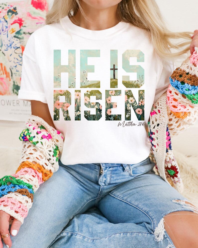 May include: White t-shirt with a floral design that spells out "He is Risen" with the scripture reference "Matthew 28:6".