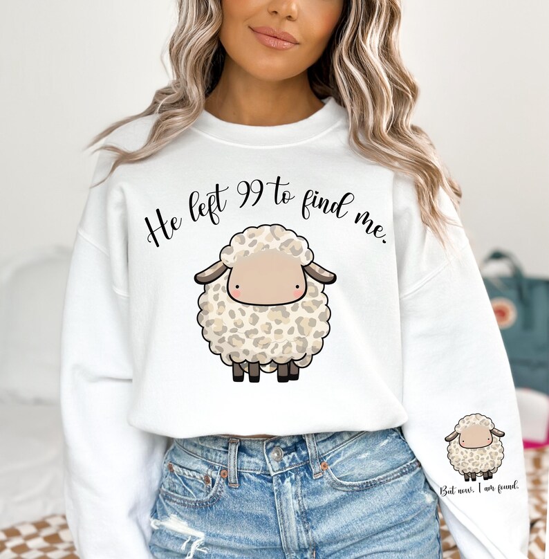 K&ouml;nnte beinhalten: Wei&szlig;er Pullover mit einem niedlichen Comic-Schaf und dem Text "He left 99 to find me." Das Schaf hat ein braunes Gesicht und ein Leopardenmuster. Der Text ist in Schwarz.