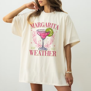 May include: A white t-shirt with a pink margarita graphic and the text "Margarita Weather" with the words "Est. 1862" underneath.
