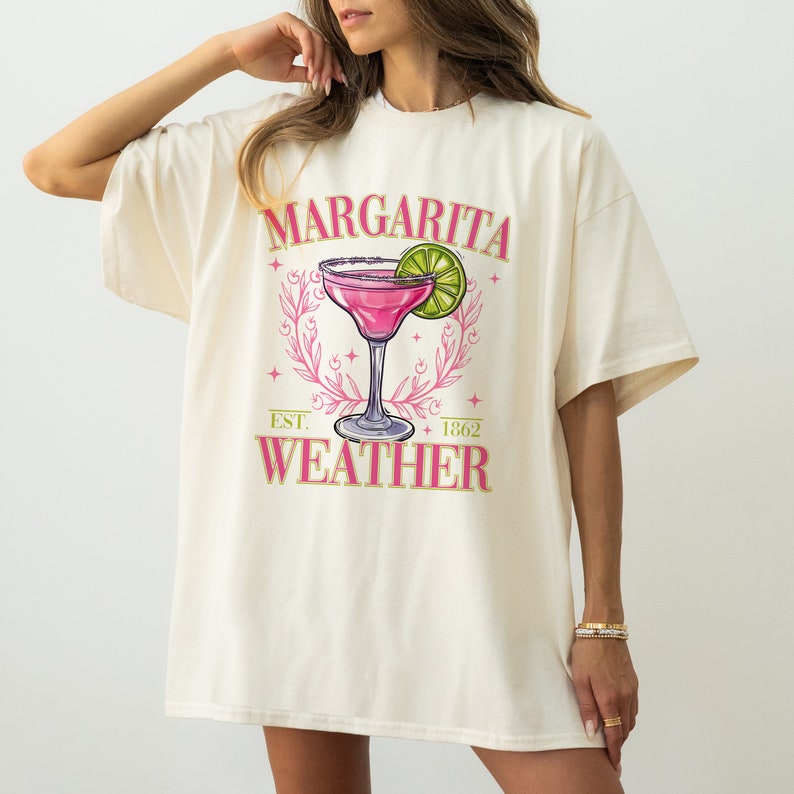 May include: A white t-shirt with a pink margarita graphic and the text "Margarita Weather" with the words "Est. 1862" underneath.