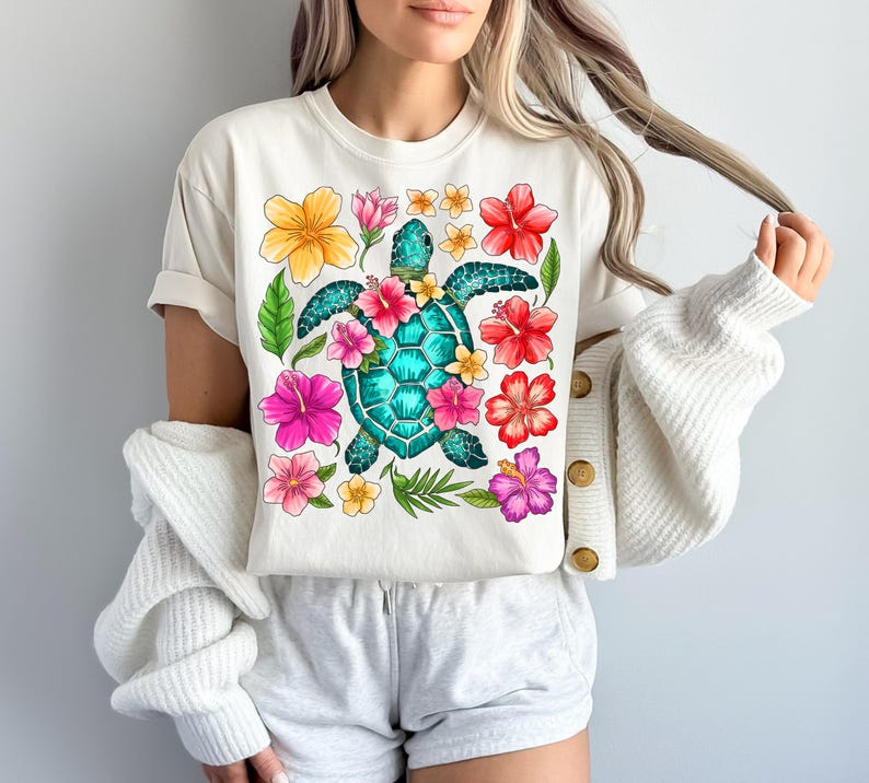 May include: White t-shirt with a colourful floral design featuring a green sea turtle with a blue shell. The flowers are pink, red, yellow, and orange.