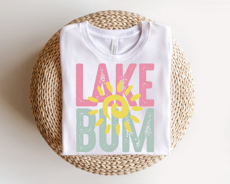 Op de afbeelding: Wit T-shirt met een roze, gele en groene afbeelding met de tekst "Lake Bum".