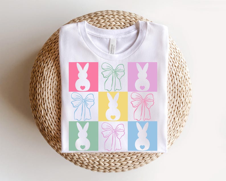 May include: White t-shirt with a colorful design of bunnies and bows. The bunnies are pink, green, blue, and yellow. The bows are pink, blue, green, and yellow.