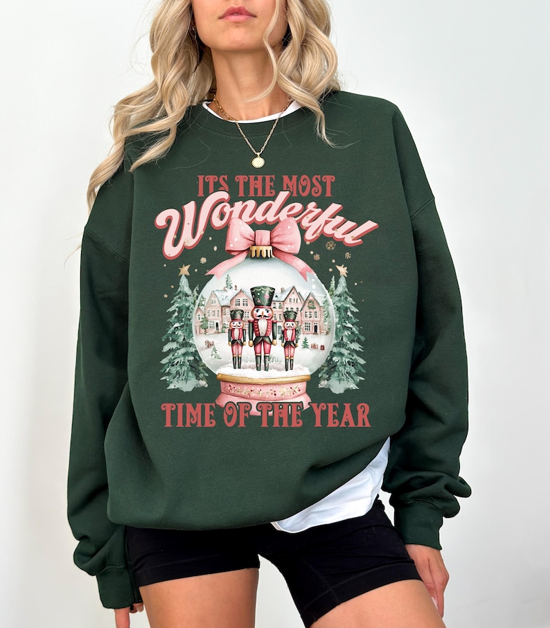 May include: Green Christmas sweatshirt with a pink and white bauble design. The bauble features three nutcracker figures and the text "It's the most Wonderful Time of the Year."