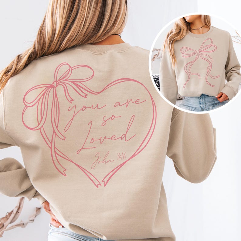 May include: A beige sweatshirt with a pink heart design on the back. The heart has a pink ribbon bow and the text "you are so loved John 3:16".