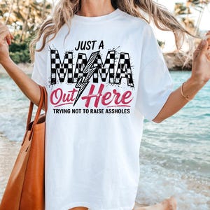 Puede incluir: Camiseta blanca con un gr&aacute;fico a cuadros blanco y negro que dice "Just a Mama Out Here Trying Not to Raise Assholes".