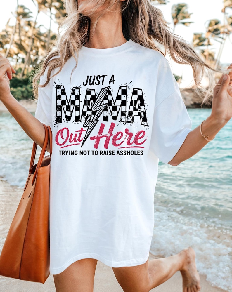 Puede incluir: Camiseta blanca con un gr&aacute;fico a cuadros blanco y negro que dice "Just a Mama Out Here Trying Not to Raise Assholes".