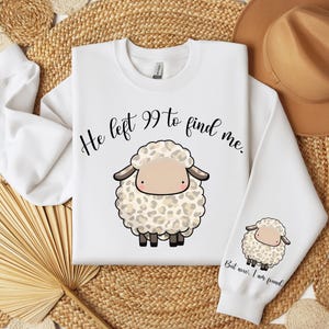 K&ouml;nnte beinhalten: Wei&szlig;er Pullover mit einer schwarz-wei&szlig;en Illustration eines Schafes mit dem Text "He left 99 to find me." Der untere Teil des Pullovers hat den Text "But now I am found."