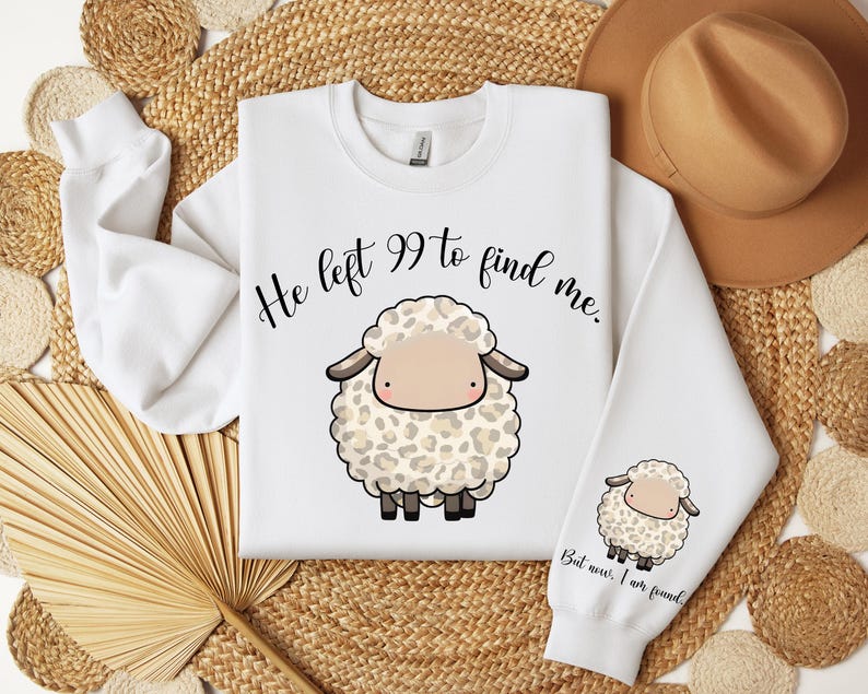 K&ouml;nnte beinhalten: Wei&szlig;er Pullover mit einer schwarz-wei&szlig;en Illustration eines Schafes mit dem Text "He left 99 to find me." Der untere Teil des Pullovers hat den Text "But now I am found."