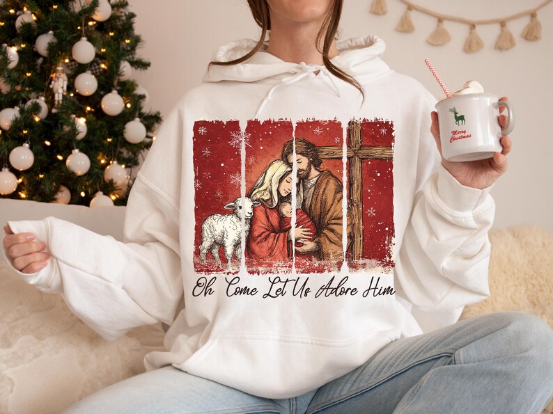 May include: White hoodie featuring a religious illustration with a lamb, a family, and a cross against a red backdrop. The text "Oh Come Let Us Adore Him" is printed below the image. A Christmas tree is in the background.
