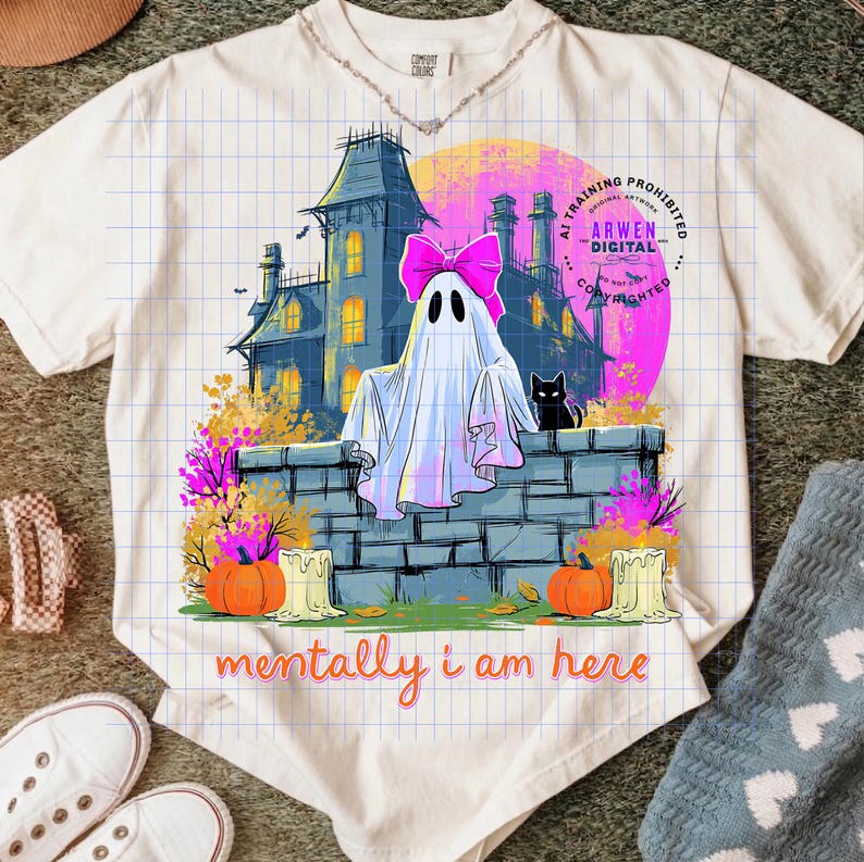 Puede incluir: Una camiseta color crema con un gr&aacute;fico de un fantasma con un lazo rosa, un gato negro, una casa encantada, calabazas y velas. El texto "mentally i am here" est&aacute; impreso en naranja en la parte inferior. El dise&ntilde;o incluye una cuadr&iacute;cula.