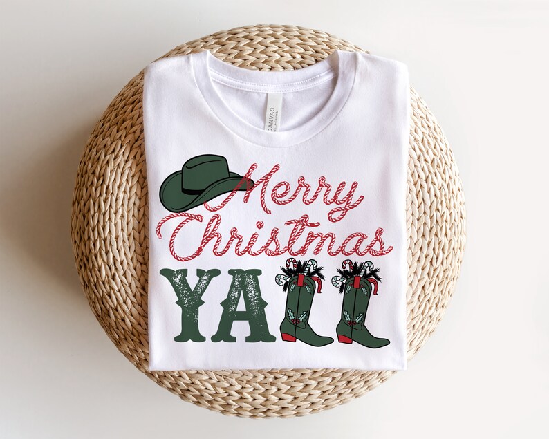 May include: White t-shirt with a festive design. The shirt features the text "Merry Christmas Y'all" in red and green, along with a green cowboy hat and boots. The boots are decorated with candy canes and holly.