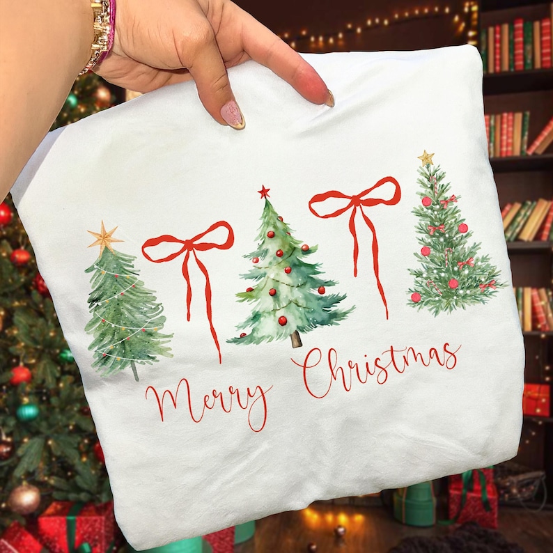 May include: White pillowcase featuring watercolor Christmas trees with red bows and ornaments. The words "Merry Christmas" are written in red script below the trees. The pillowcase is held up by a hand.