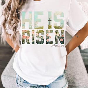 May include: White t-shirt with a floral design that spells out "He is Risen" with a cross and the text "Matthew 28:6".