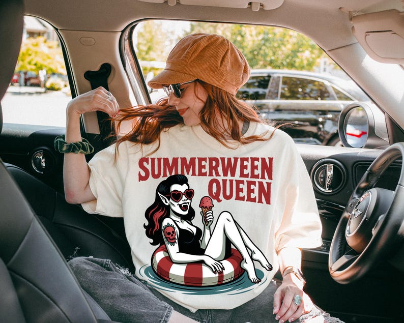May include: Cream-colored t-shirt with the text "SUMMERWEEN QUEEN" in red. The graphic features a vampire woman in a swimsuit, heart-shaped sunglasses, and a tattoo, holding an ice cream cone while floating on a red and white striped inner tube.
