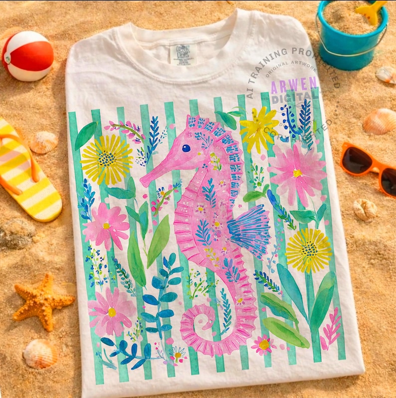 May include: White t-shirt featuring a pink seahorse design with floral accents and vertical green stripes. The seahorse is surrounded by colorful flowers and foliage. The shirt is displayed on a sandy surface with beach-themed accessories.