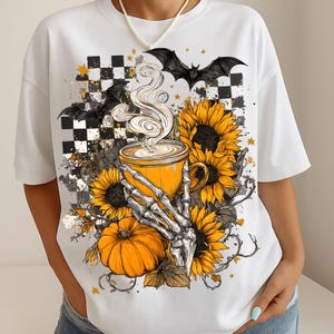 K&ouml;nnte beinhalten: Wei&szlig;es T-Shirt mit einem Halloween-Motiv. Das Design zeigt eine gelbe Kaffeetasse, Sonnenblumen, einen K&uuml;rbis und eine Skeletthand. Schwarze Flederm&auml;use und ein Schachbrettmuster vervollst&auml;ndigen das Design.