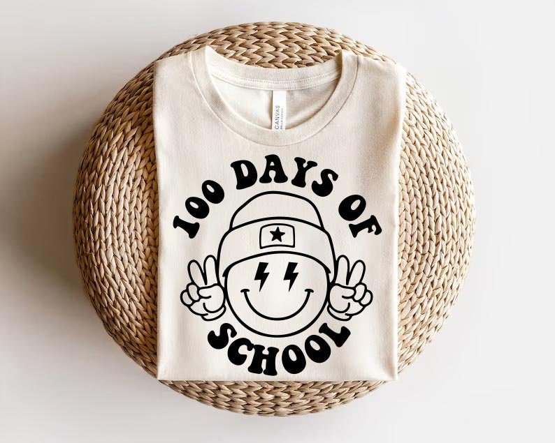 May include: A white t-shirt with a black graphic design that says "100 Days of School" with a smiley face wearing a hat and peace signs.
