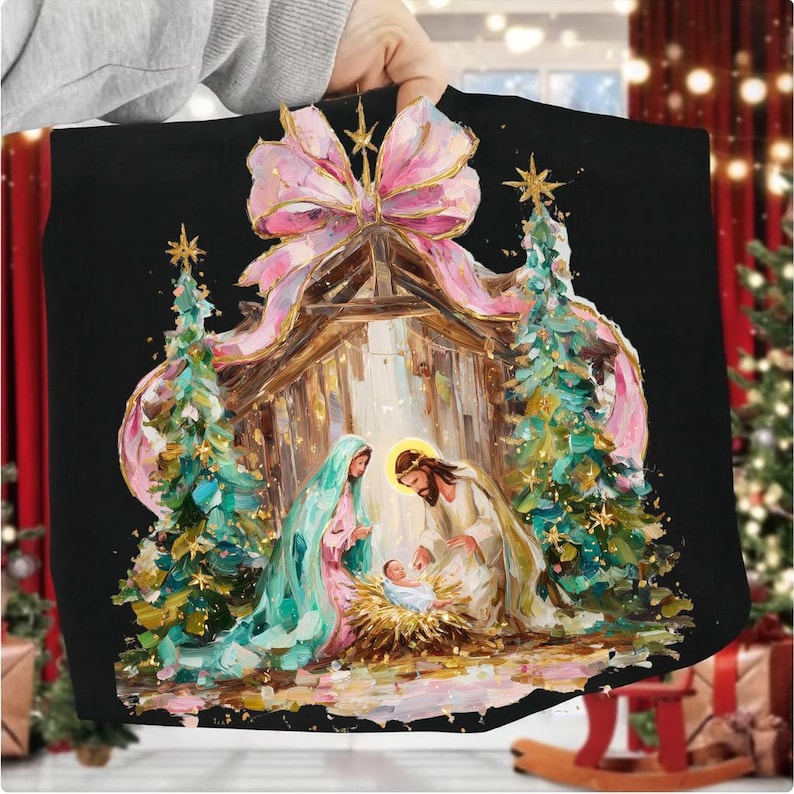 May include: Black Christmas-themed artwork featuring a Nativity scene with Mary, Joseph, and baby Jesus in a manger. The image includes a large pink bow, Christmas trees, and gold accents. The artwork is held by a person.