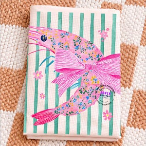 May include: A folded pink and white striped fabric with a large pink shrimp illustration. The shrimp is decorated with a floral pattern and a large pink bow. Green stripes and small pink flowers accent the design.