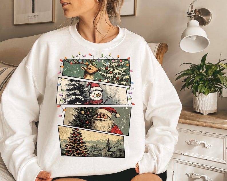 May include: White sweatshirt featuring a Christmas-themed graphic. The design includes panels with a reindeer, snowman, and Santa Claus, along with a Christmas tree and a church. The graphic is framed by a string of colorful lights.