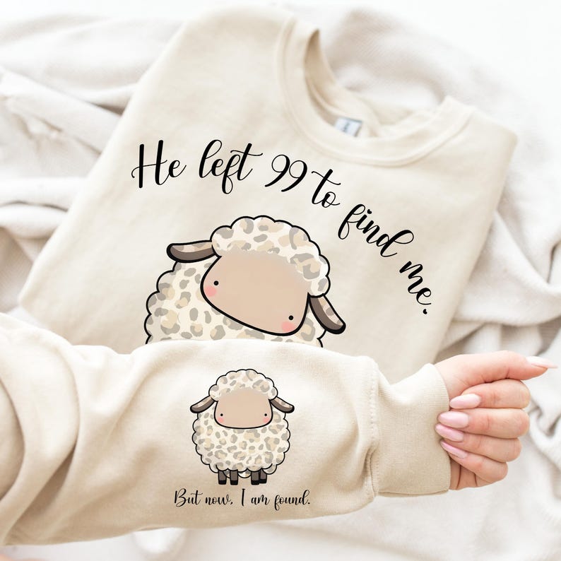 K&ouml;nnte beinhalten: Ein beiger Pullover mit einem niedlichen Cartoon-Schaf, das ein Leopardenmuster tr&auml;gt. Der Text "He left 99 to find me." ist &uuml;ber dem Schaf gedruckt und der Text "But now, I am found." ist unter dem Schaf gedruckt.