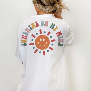 May include: White t-shirt with a colorful graphic of a smiling sun and the text "Sunshine on my mind".