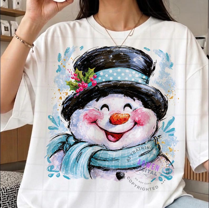 May include: A white t-shirt featuring a graphic illustration of a smiling snowman wearing a black top hat with a light blue polka dot band, a light blue scarf, and a sprig of holly with red berries, accented by blue paint-like splashes.