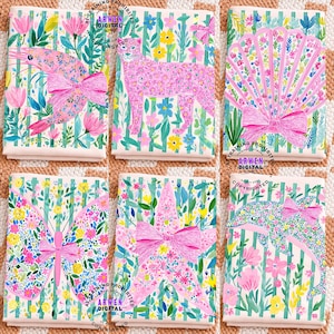 May include: Six notebooks with animal and floral designs. Each notebook features a different animal or shape, including a cheetah, butterfly, and dolphin, all adorned with pink bows. The backgrounds have a floral pattern.