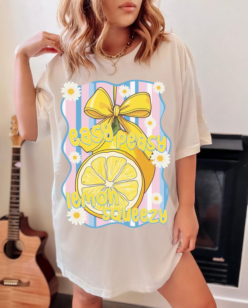 Pu&ograve; includere: Maglietta bianca con una grafica di un limone giallo con un fiocco giallo e il testo "easy peasy lemon squeezy" in lettere blu e rosa.