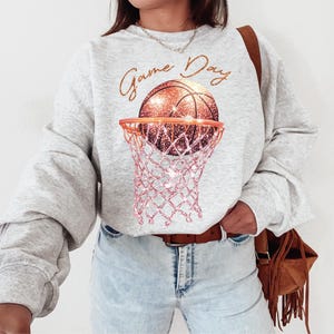 May include: A gray sweatshirt with the text "Game Day" and a glittery orange basketball in a pink net.