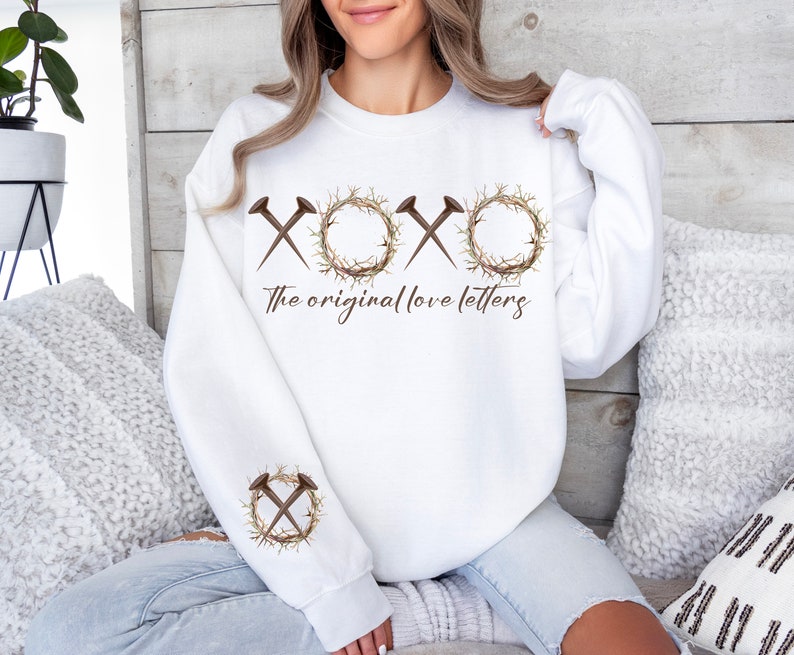 May include: White sweatshirt with a graphic of a crown of thorns and nails forming the letters "XOXO" with the text "The original love letters" below.